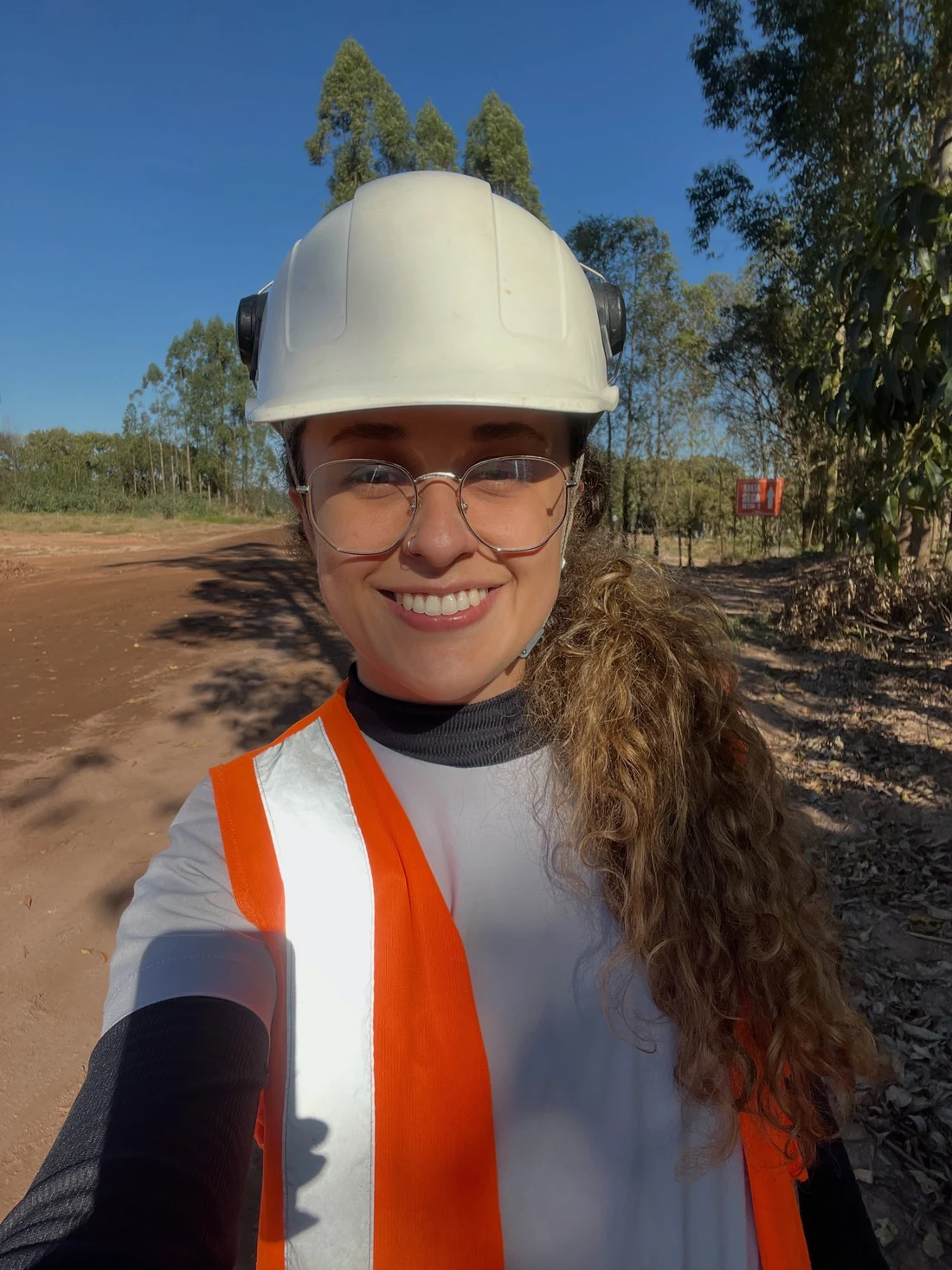 Camila Abreu em campo, usando capacete branco e colete de segurança.